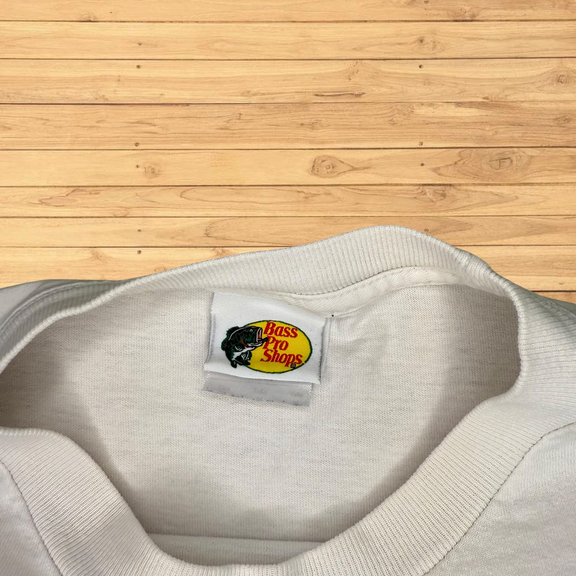 Gray sweatshirt with a Bass Pro Shops logo tag on a wooden surface